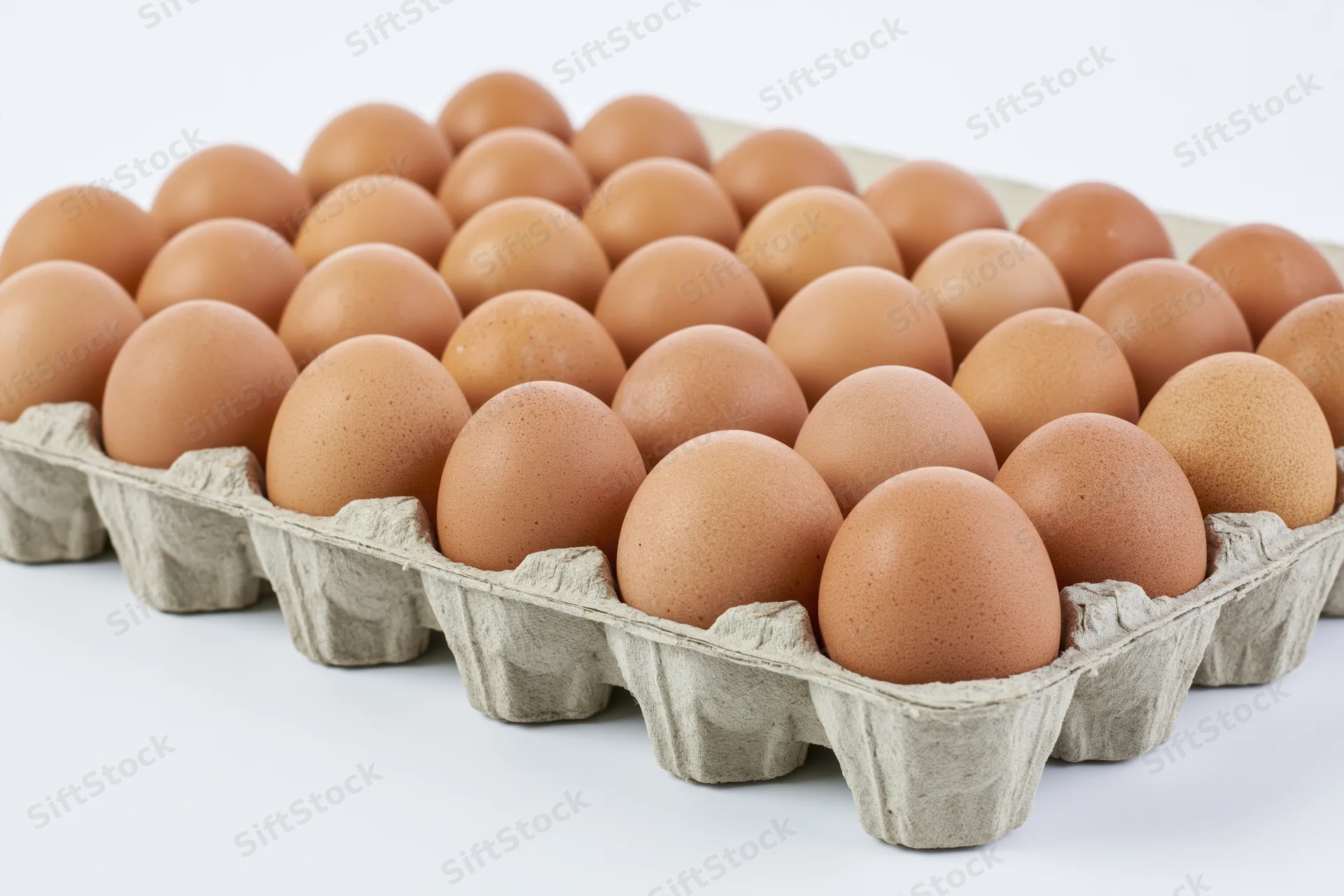 Thirty brown chicken eggs arranged in a flat cardboard tray on a white surface