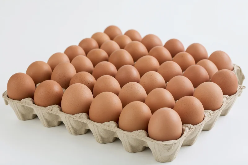 Thirty brown chicken eggs arranged in a flat cardboard tray on a white surface
