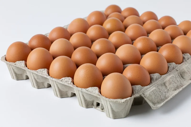 Thirty brown chicken eggs arranged in a flat cardboard tray on a white surface