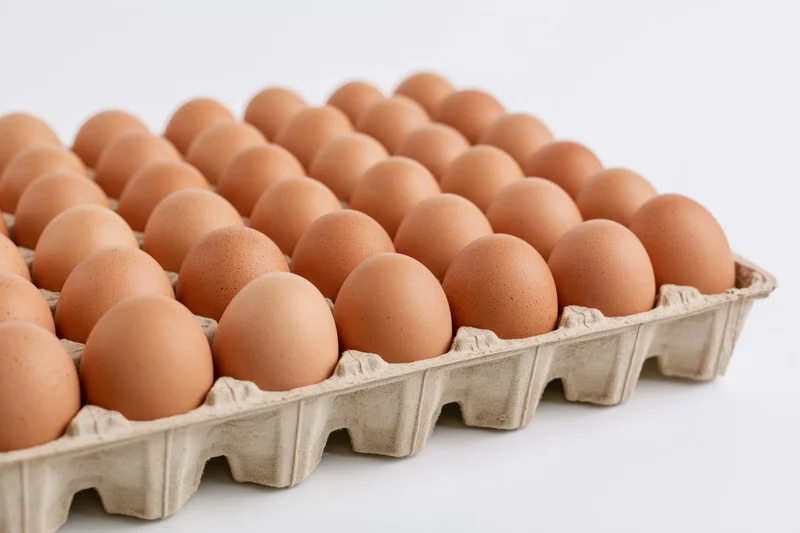 Thirty brown chicken eggs arranged in a flat cardboard tray on a white surface