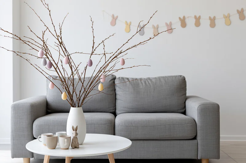 Easter decoration with bare branches and pastel eggs in a vase on a coffee table in front of a gray sofa