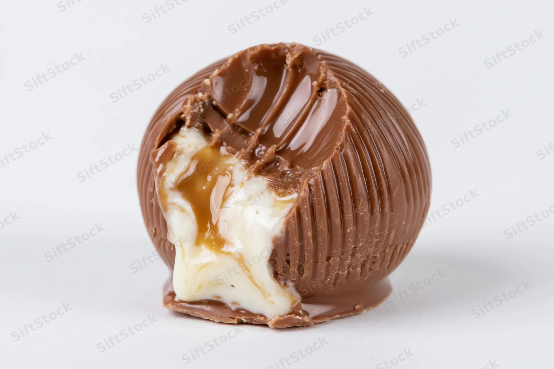 Milk chocolate truffle with bite taken out revealing creamy caramel and white chocolate filling on white background