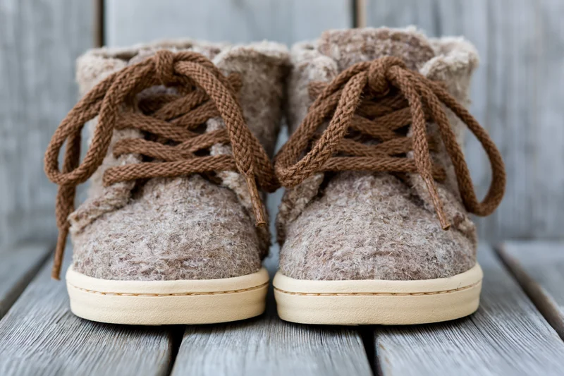 Pair of rustic lace-up ankle boots made from textured wool felt with brown cord laces on a wooden deck
