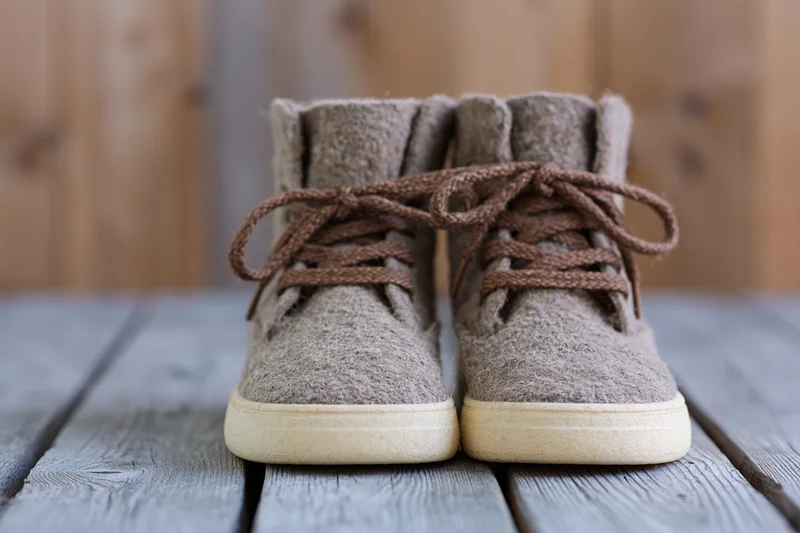 Pair of rustic lace-up ankle boots made from textured wool felt resting on weathered wooden deck
