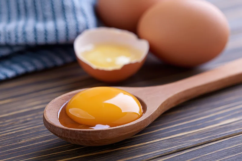 Raw egg yolk in wooden spoon on dark wood table