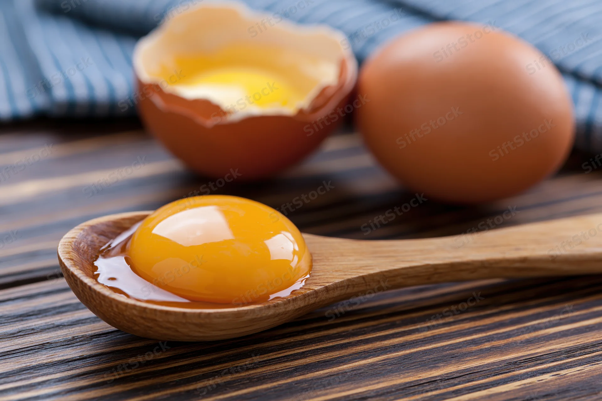 Raw egg yolk in wooden spoon on dark wood table