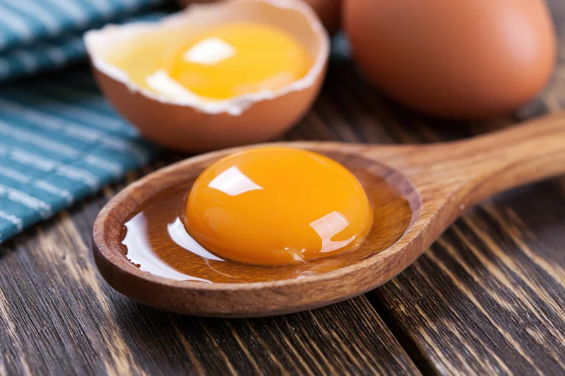Raw egg yolk in wooden spoon on dark wood table