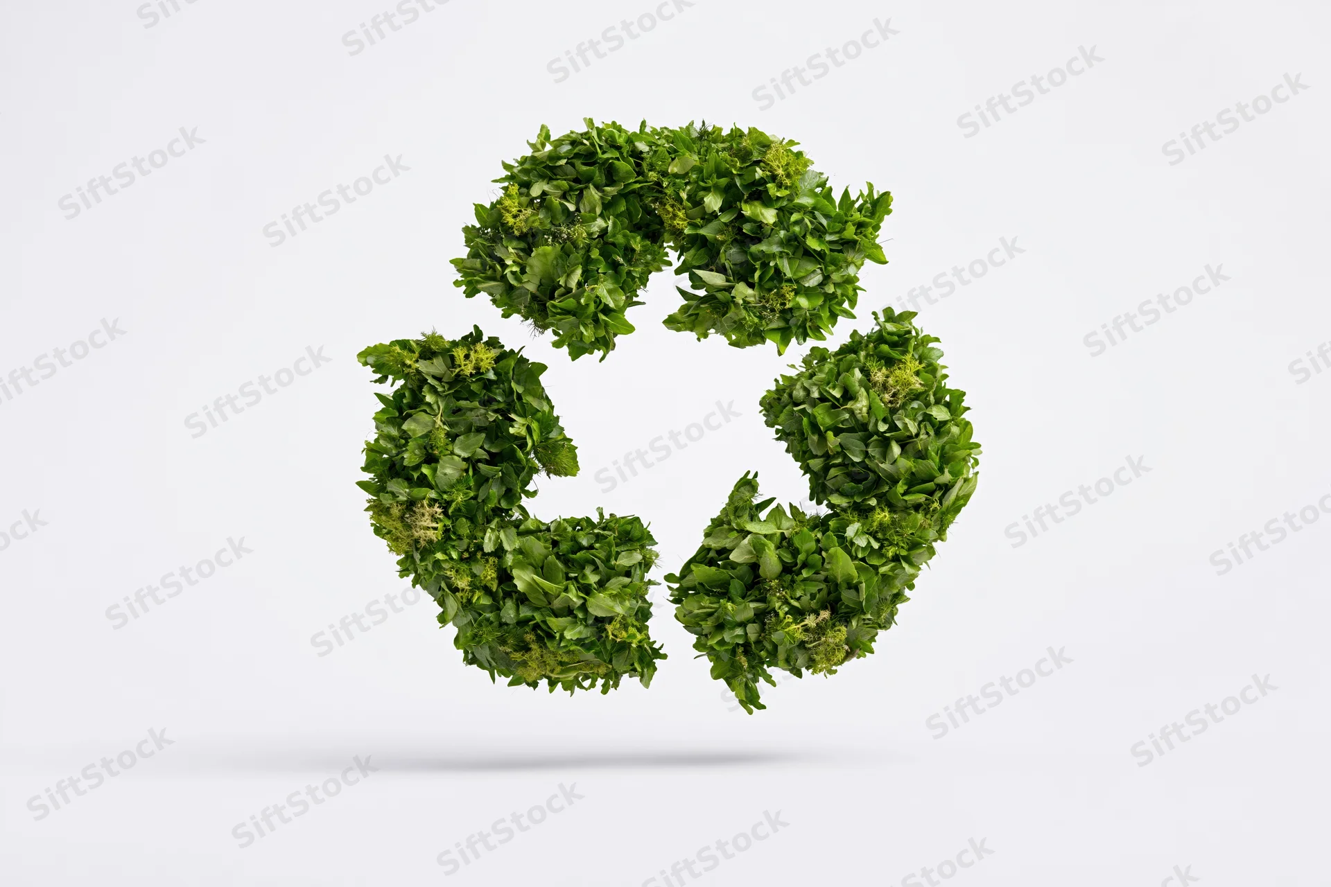 Recycling symbol formed from dense green leaves floating against white background