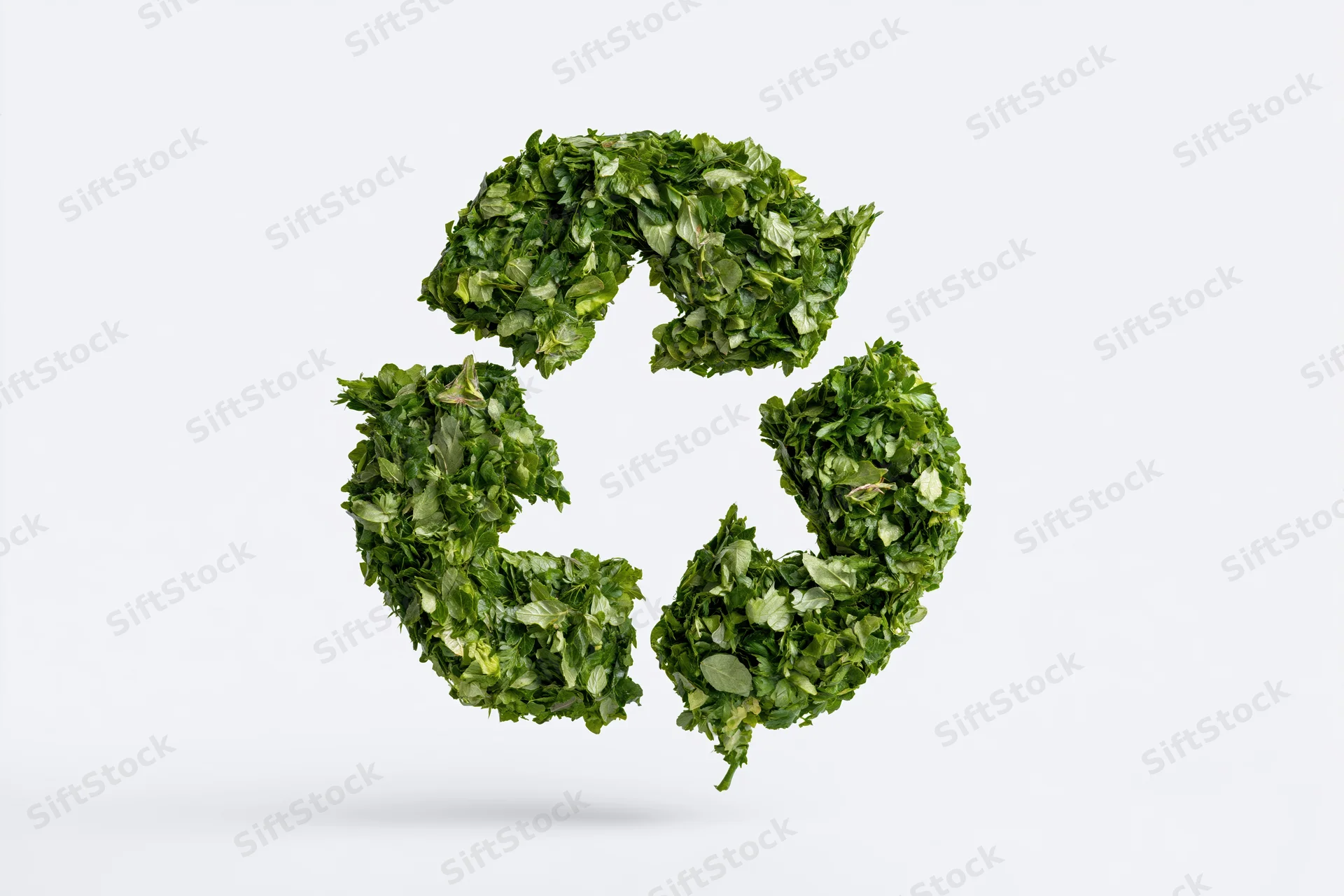 Recycling symbol formed from dense green leaves floating against white background