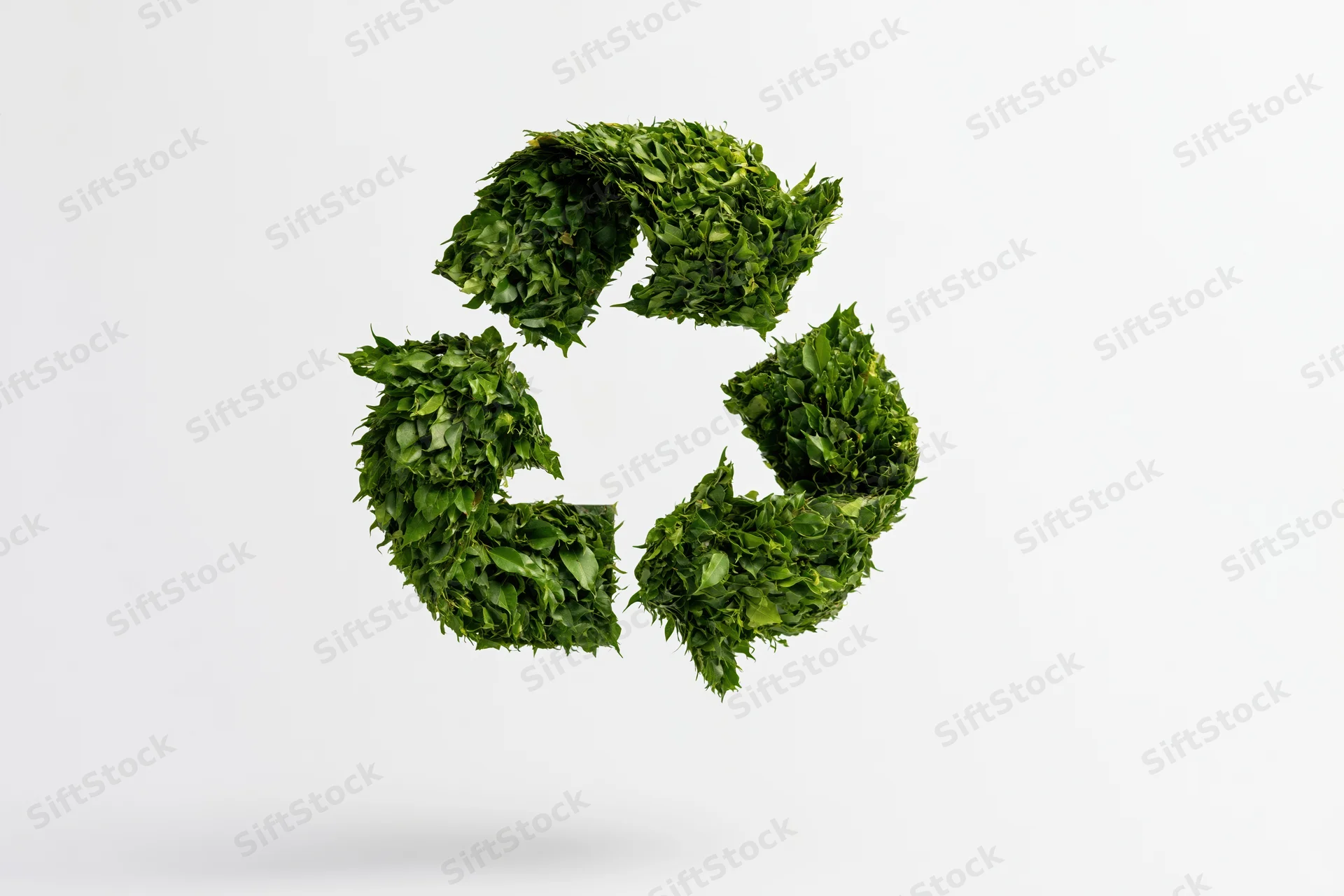 Recycling symbol formed from dense green leaves floating against a white background