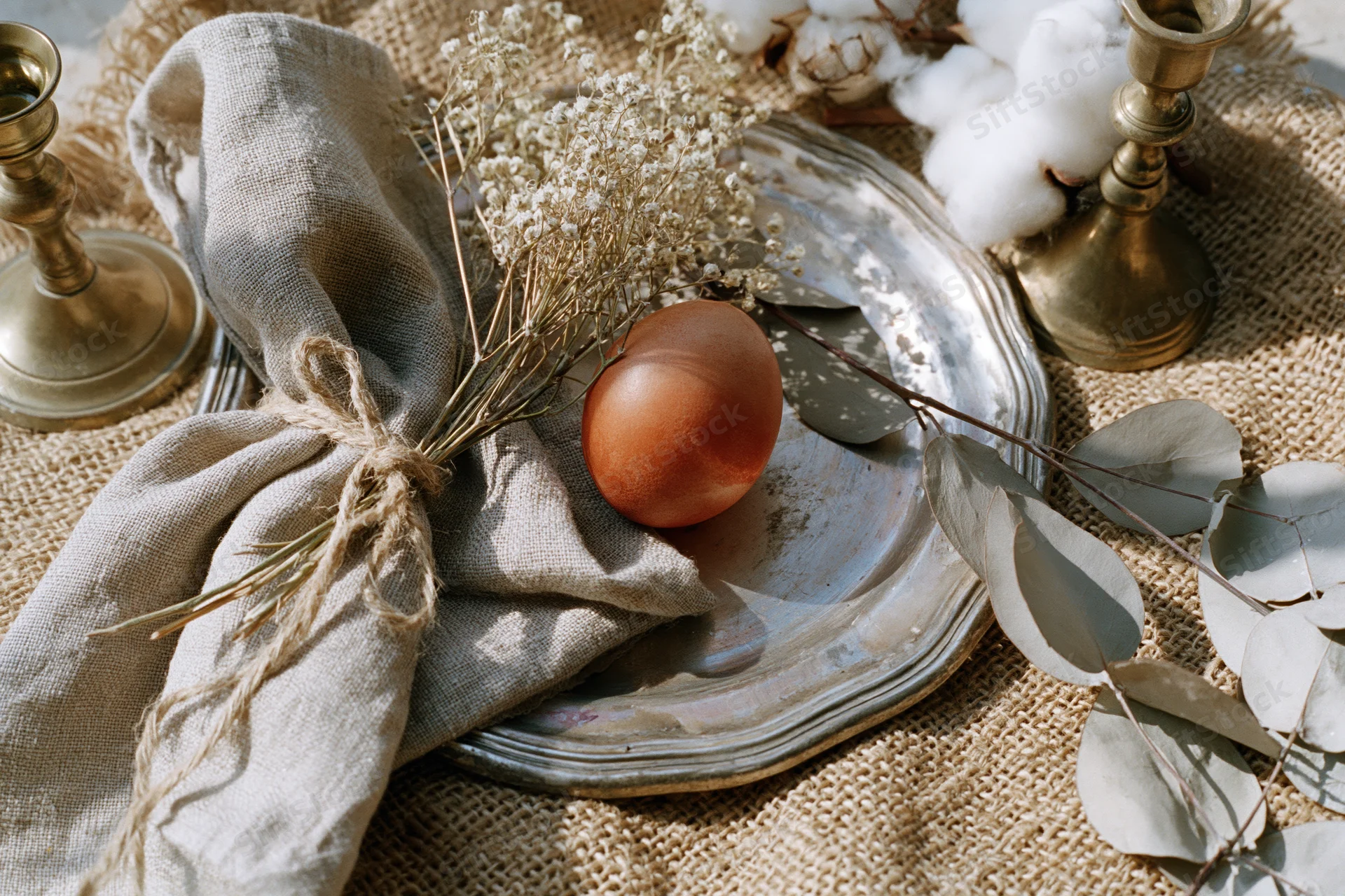 Terracotta-dyed egg on a rustic table setting with dried flowers and linen napkin for easter spring decoration