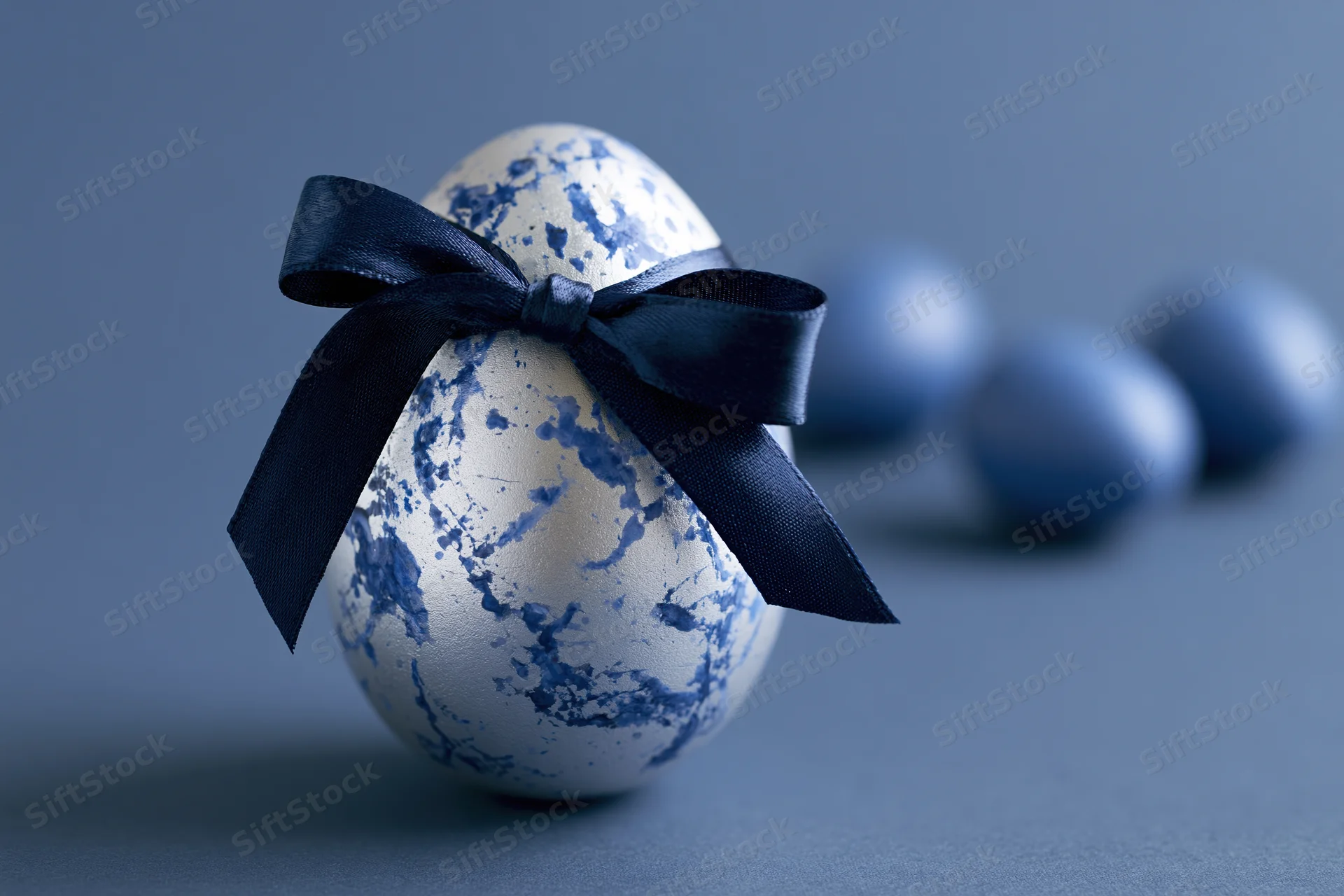 Silver easter egg with blue marbled paint splatters tied with navy ribbon on gray surface