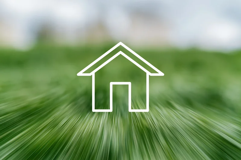 White outline icon of a small house over a blurred green grass background