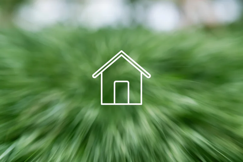 White outline house icon over blurred green foliage background
