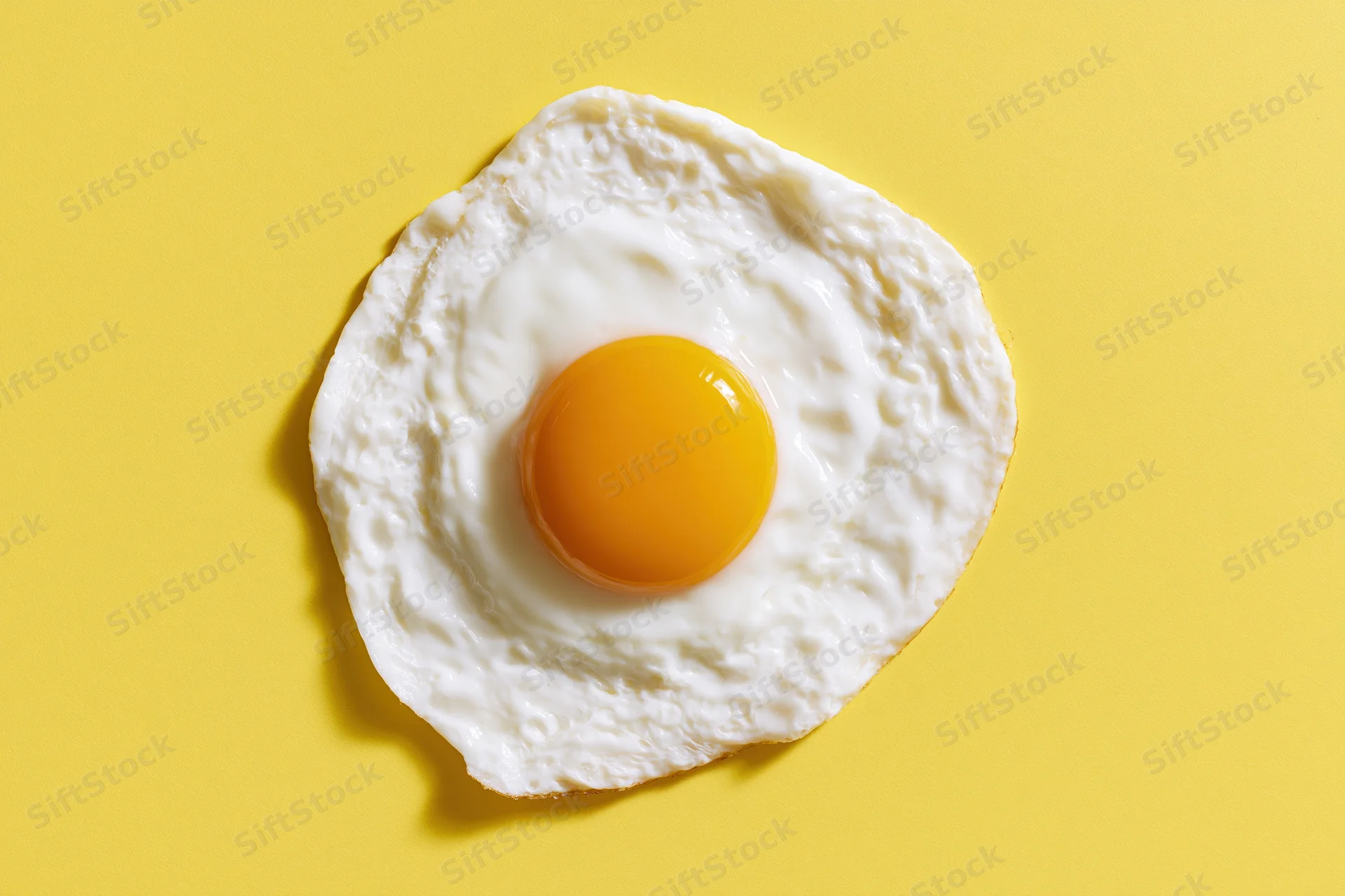 Single fried egg viewed from above on a yellow surface