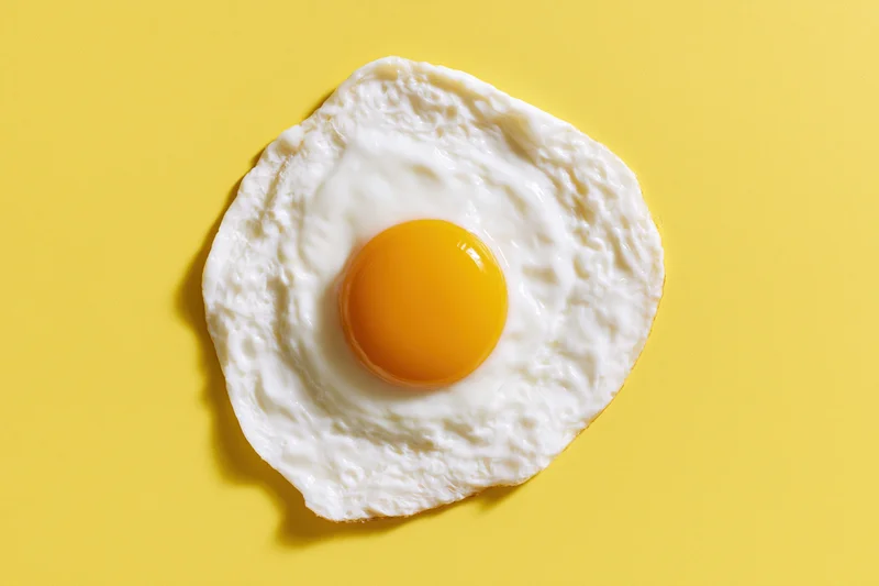 Single fried egg viewed from above on a yellow surface