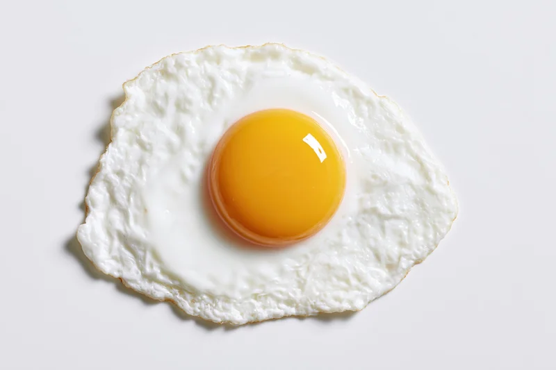 Single fried egg sunny side up on white surface overhead view