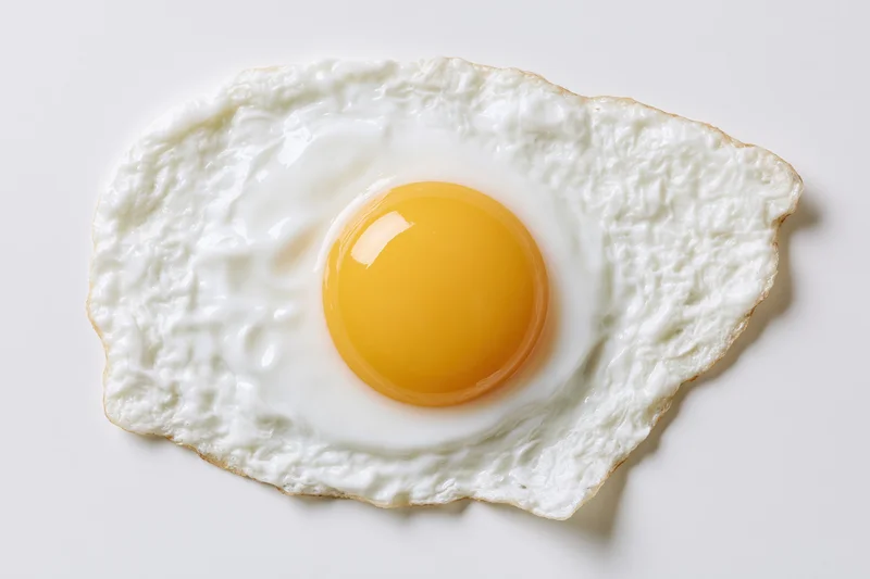 Single fried egg sunny side up on white surface overhead view