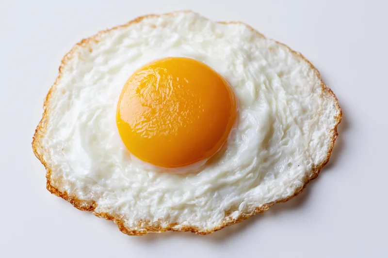 Single fried egg sunny-side up on plain white surface