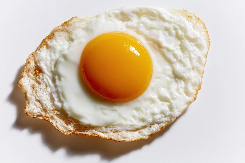 Single fried egg sunny-side up on plain white surface