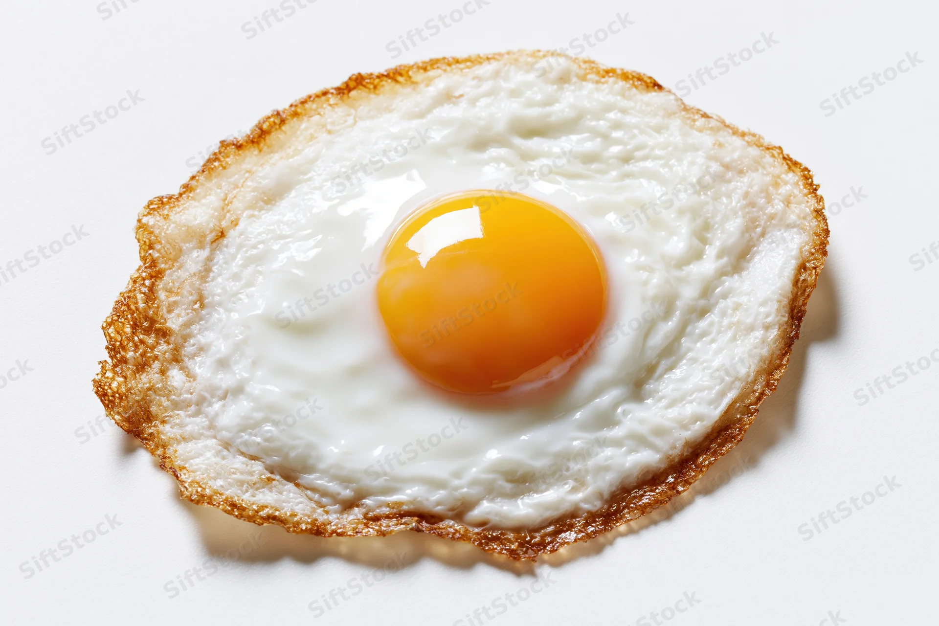 Single fried egg sunny side up with crispy lacy brown edges on white background