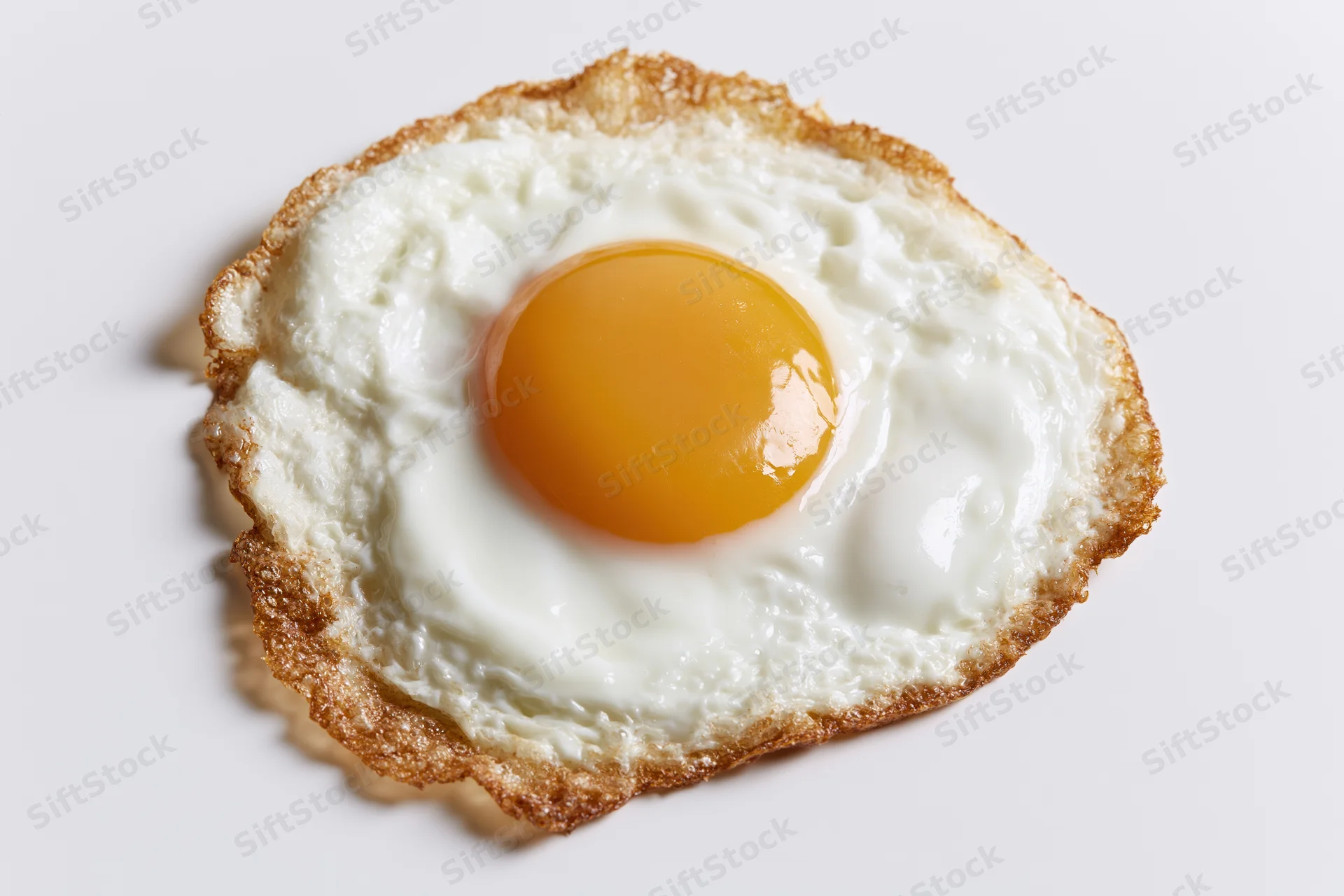 Single fried egg sunny side up with crispy lacy brown edges on white background