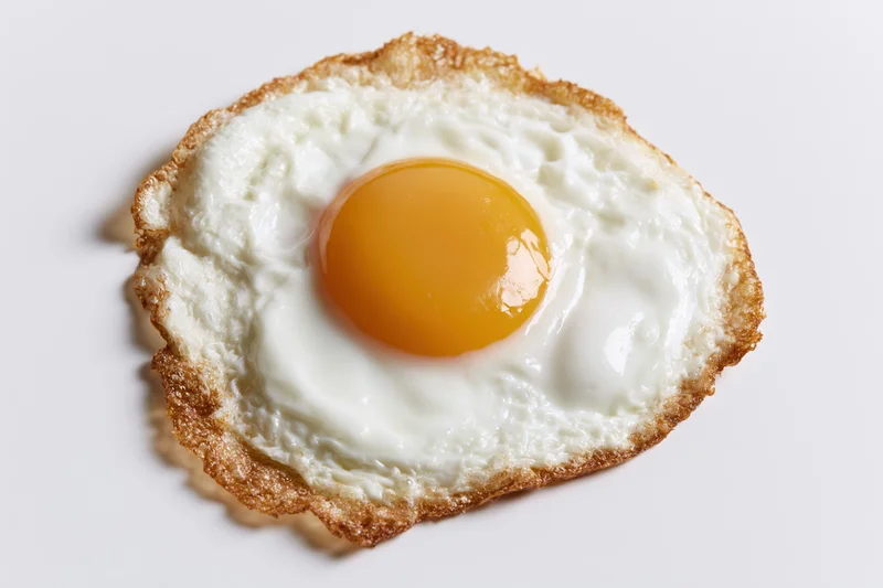 Single fried egg sunny side up with crispy lacy brown edges on white background