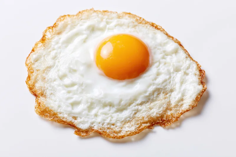 Single fried egg sunny side up with crispy lacy edges on white background
