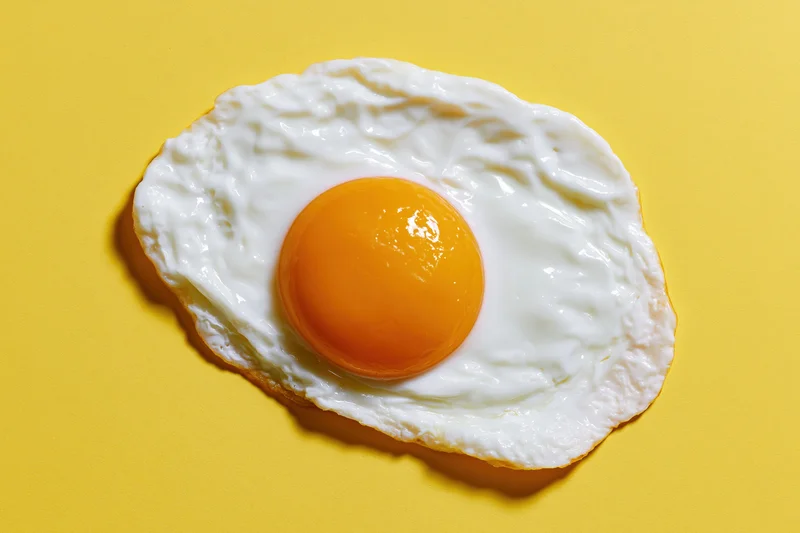 Single fried egg with domed orange yolk centered on yellow background