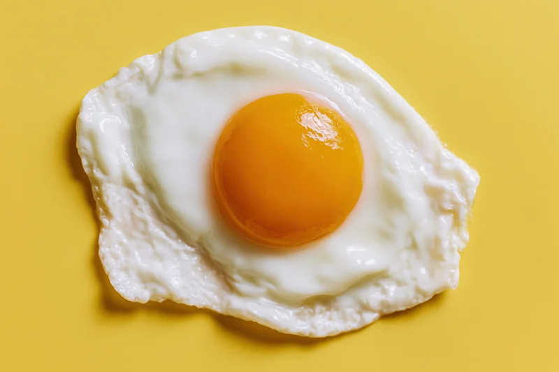 Single fried egg with domed orange-yellow yolk centered on yellow background