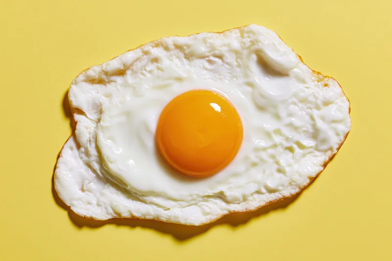 Single fried egg with domed orange yolk centered on yellow background