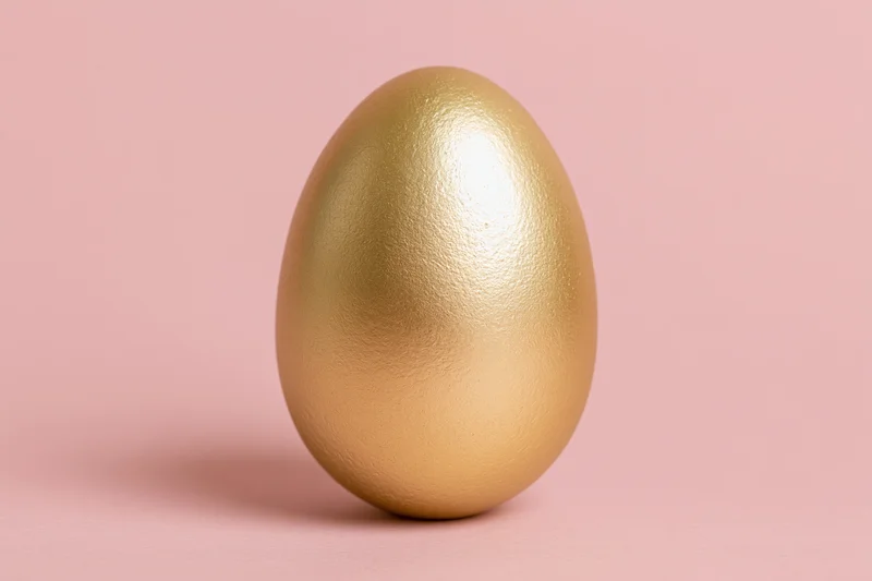 Single golden painted egg standing upright centered against a pink background
