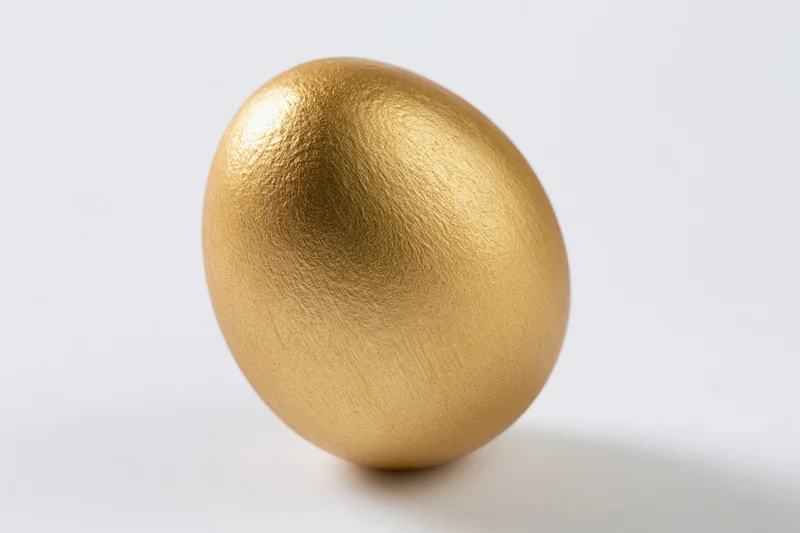Single gold-painted egg standing upright centered against a white background