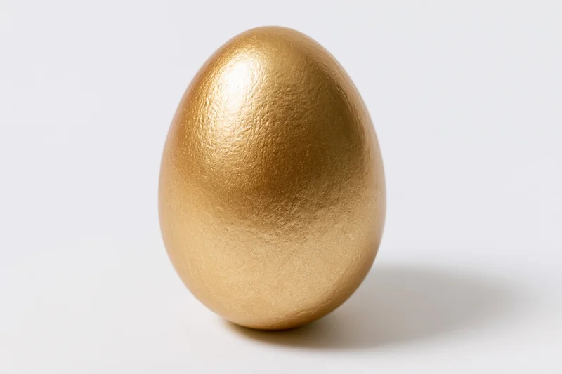 Single gold-painted egg standing upright centered against a white background