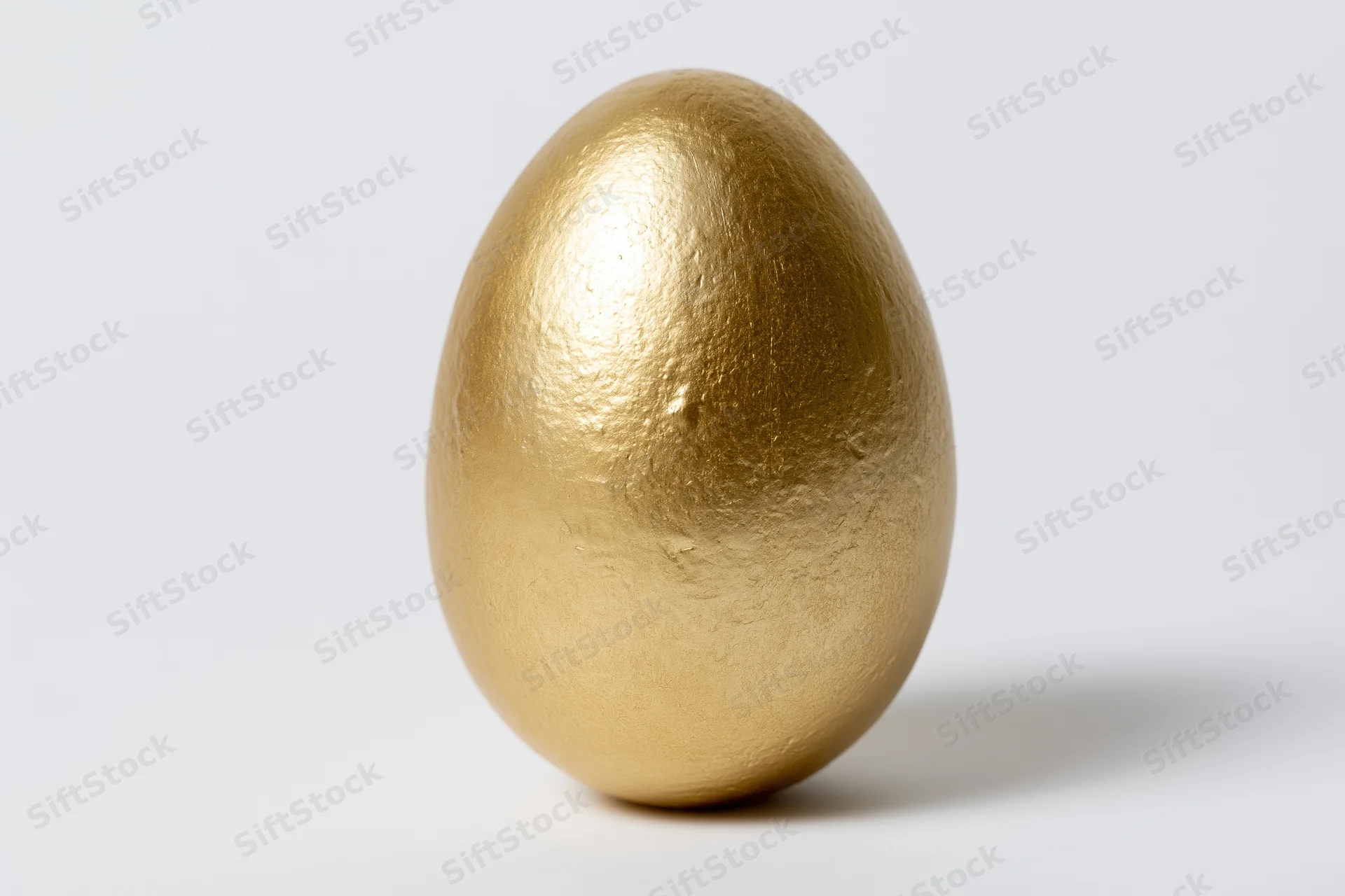 Single gold-painted egg standing upright isolated against a white background