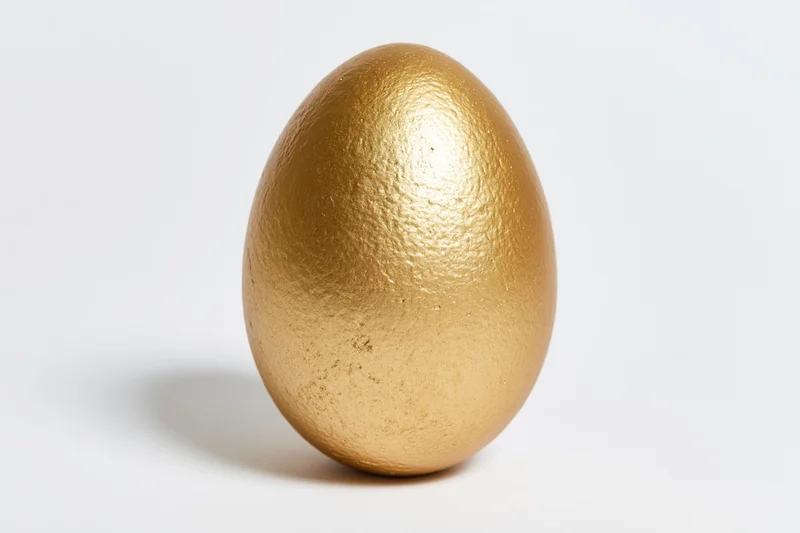Single gold-painted egg standing upright on white surface