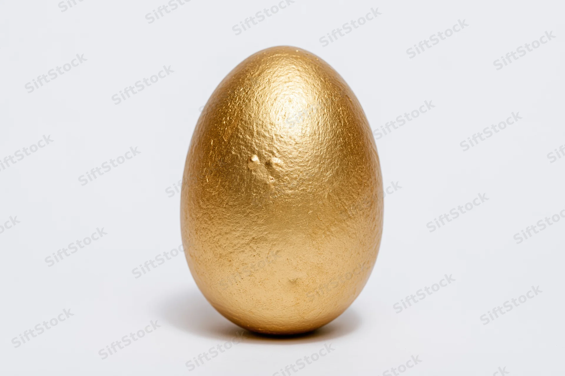 Single gold-painted egg standing upright isolated against a white background