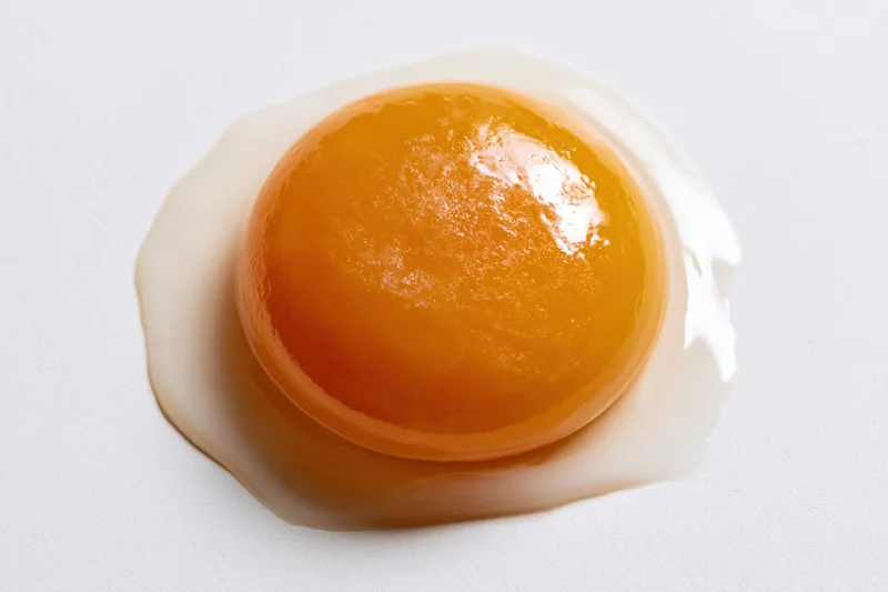 Raw egg yolk resting on white surface with surrounding egg white