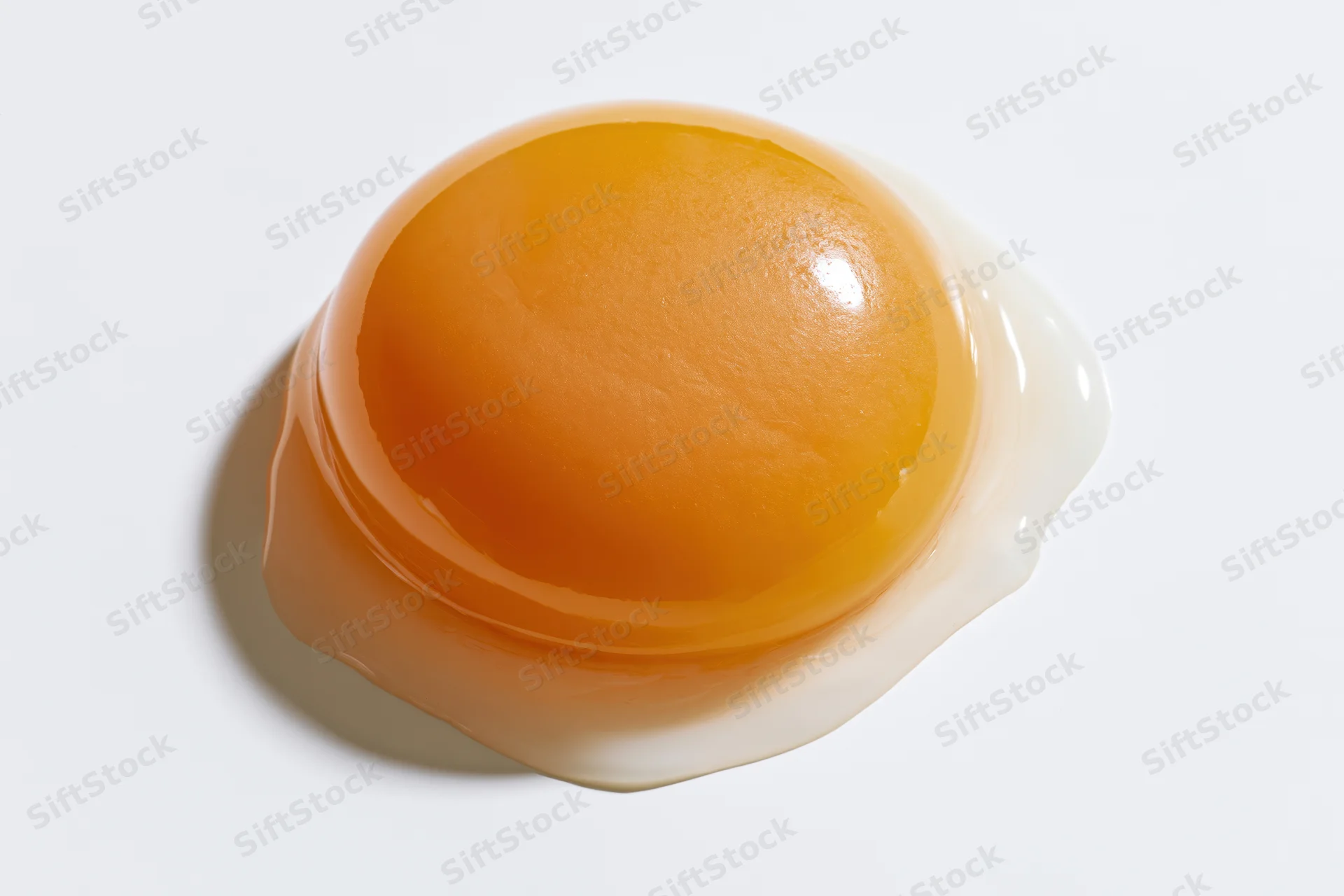 Raw egg yolk resting on white surface with surrounding egg white
