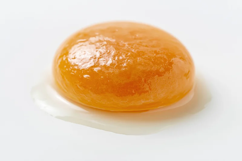 Raw egg yolk resting on a white surface with surrounding egg white