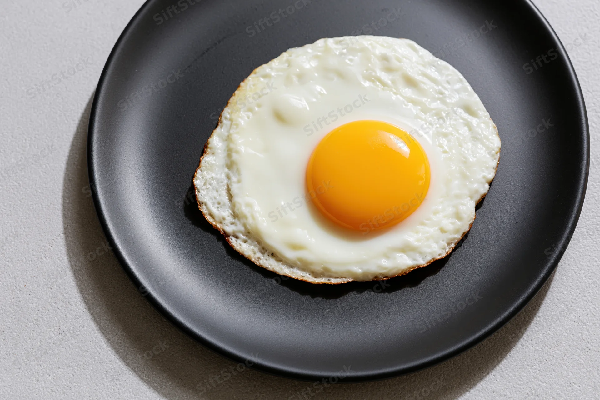 Sunny-side-up fried egg on a black plate with golden yolk and white edges, viewed from above on a gray surface