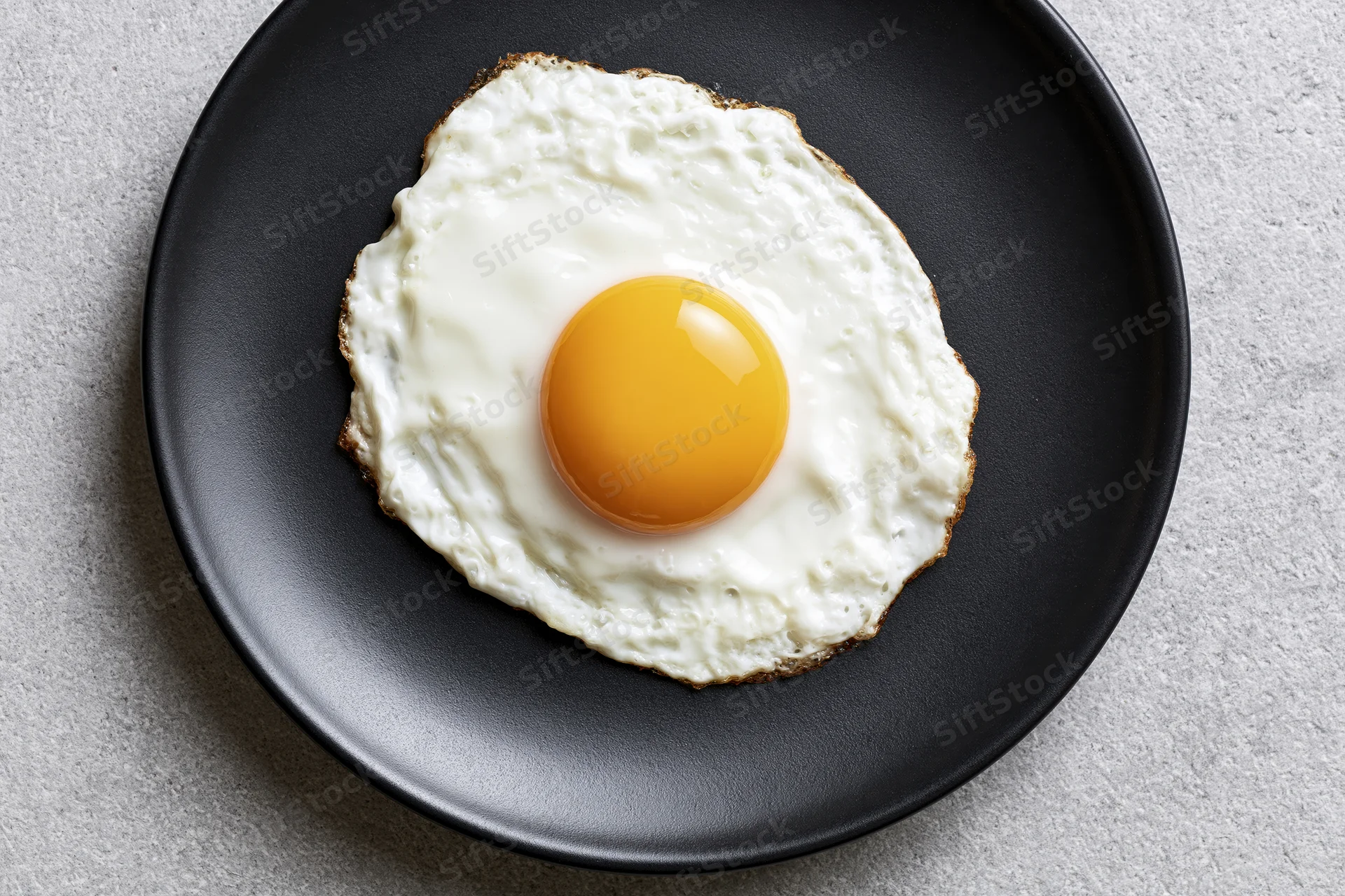 Sunny-side-up fried egg with golden yolk on black plate viewed from above