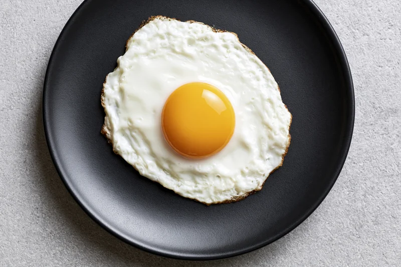 Sunny-side-up fried egg with golden yolk on black plate viewed from above