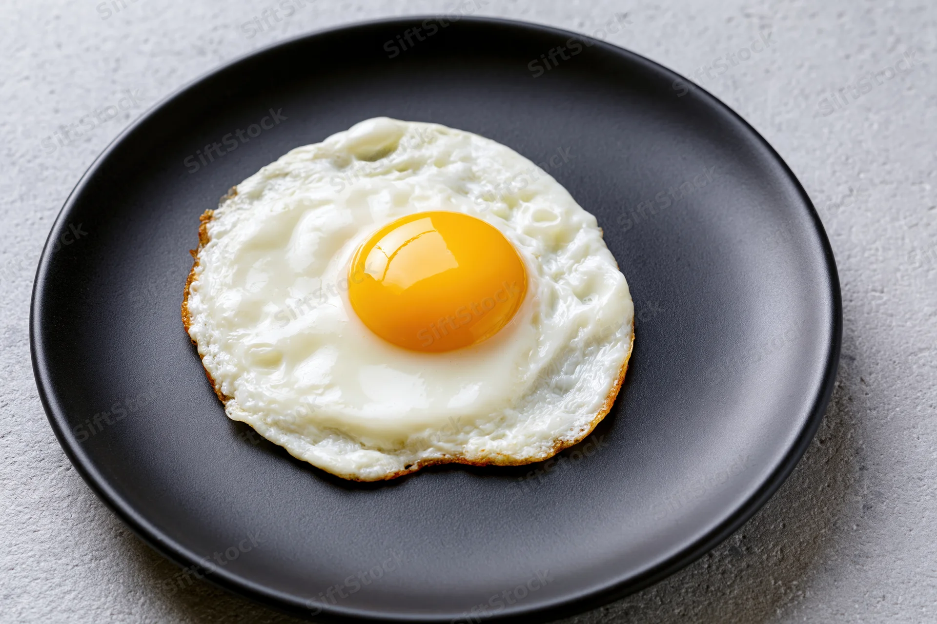 Sunny-side-up fried egg with golden yolk on black plate on gray surface
