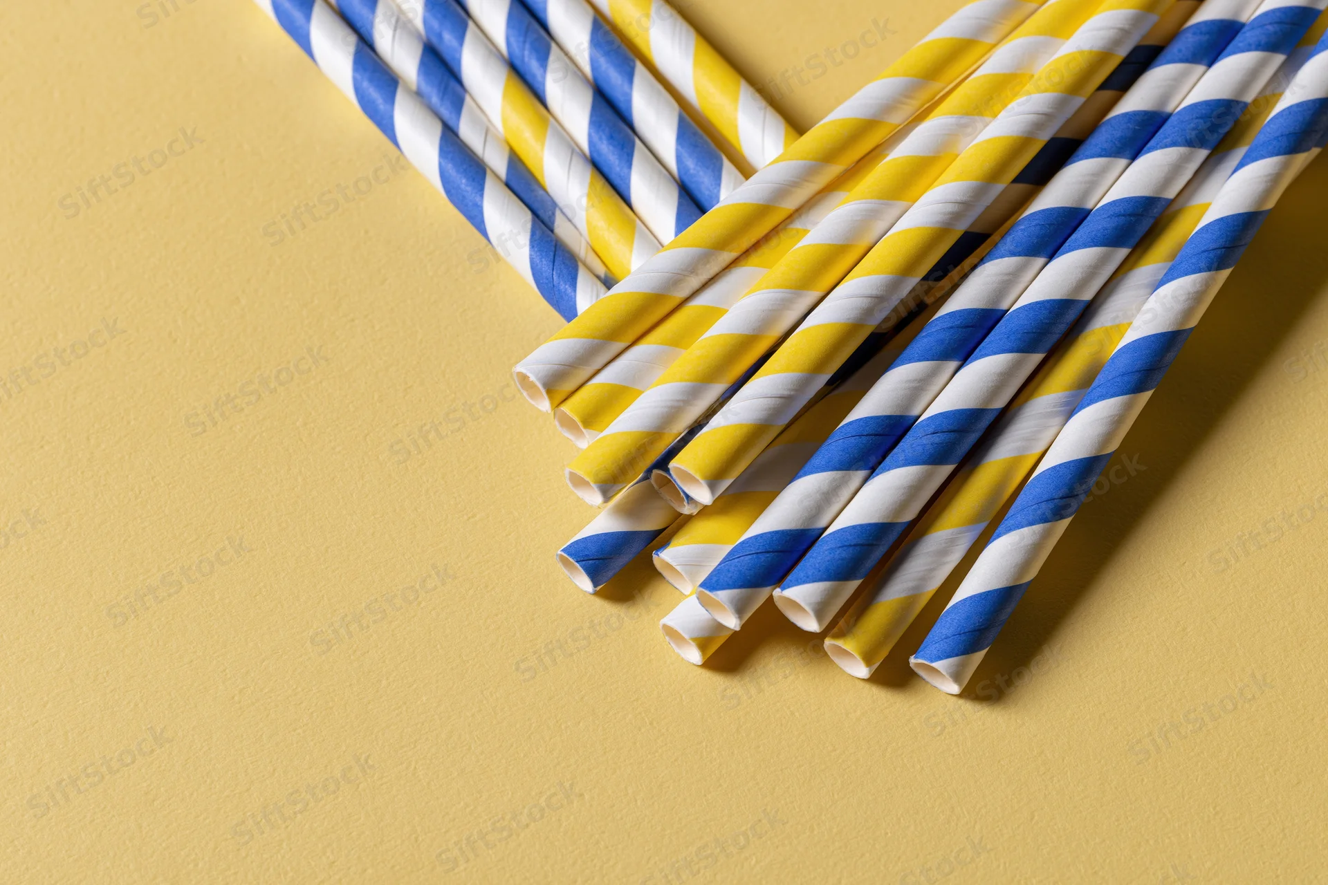 Striped paper drinking straws arranged diagonally on a yellow surface with copyspace