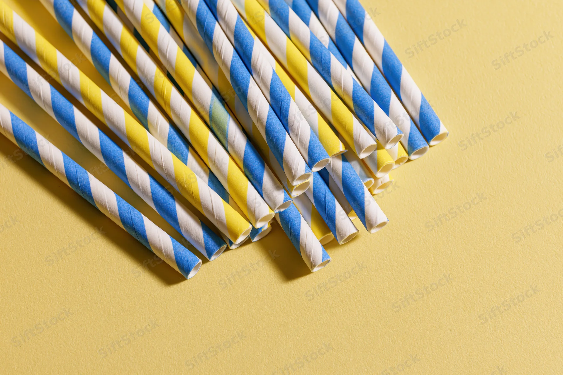 Striped paper drinking straws arranged diagonally on a yellow background with copyspace