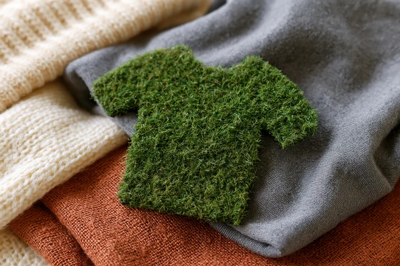 A tshirt-shaped cutout covered in green artificial grass resting on a stack of folded clothing
