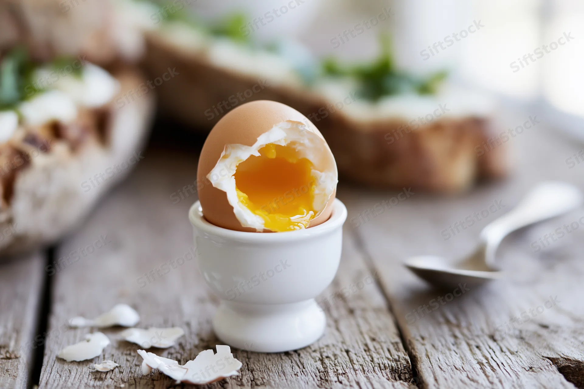 Soft-boiled egg cracked open in a white ceramic egg cup on a rustic wooden table with toast and spoon nearby