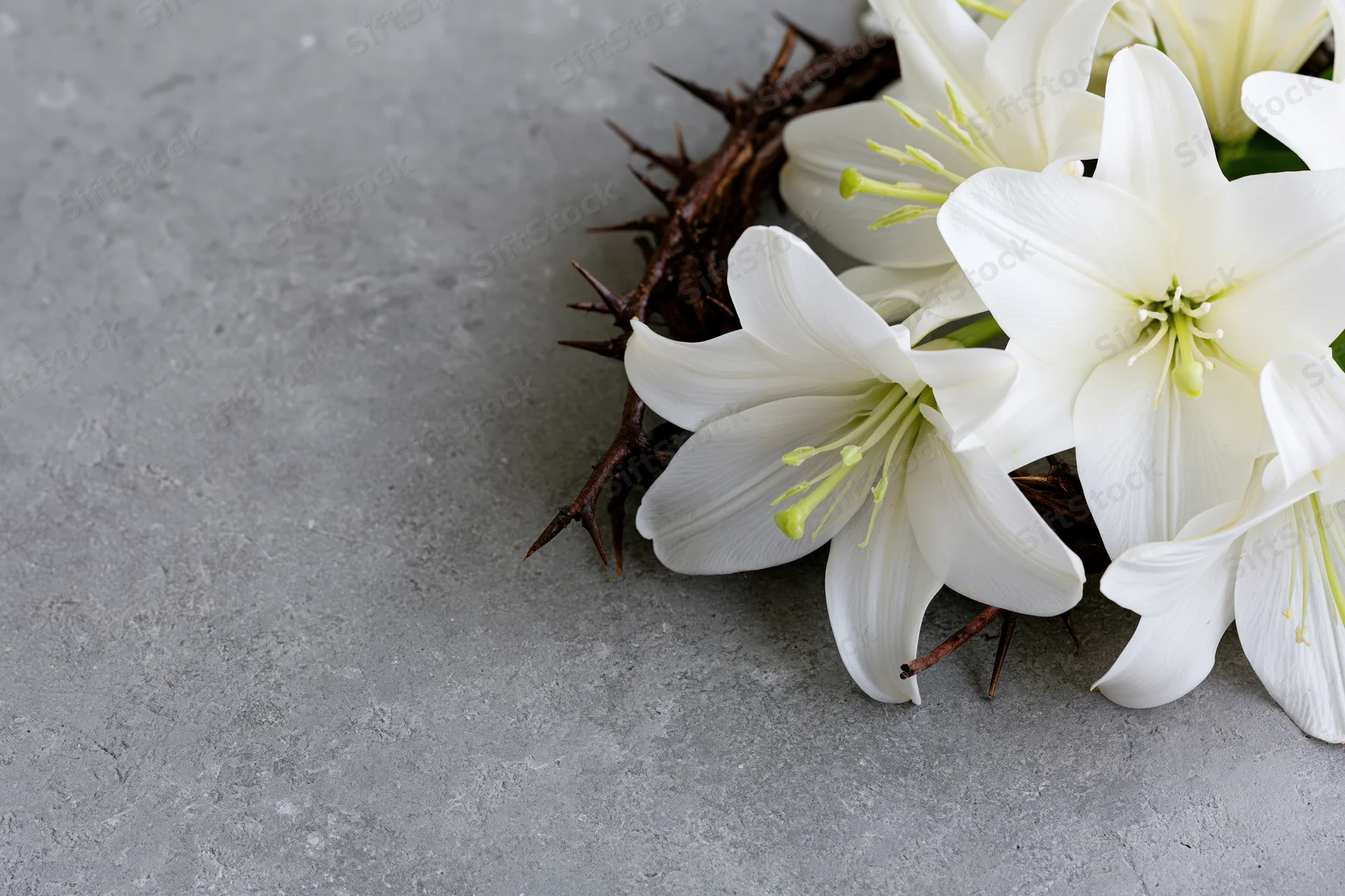 Crown of thorns with white easter lilies resting on gray concrete surface