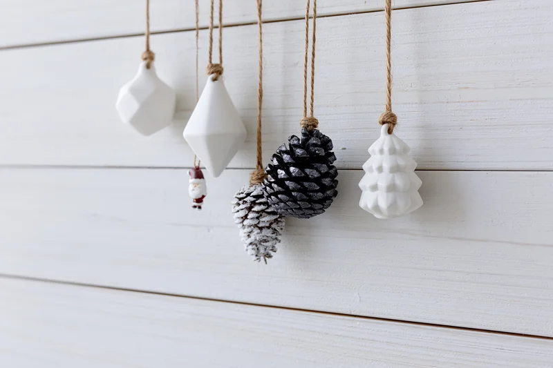 Assorted christmas ornaments hanging from twine strings against white wooden wall